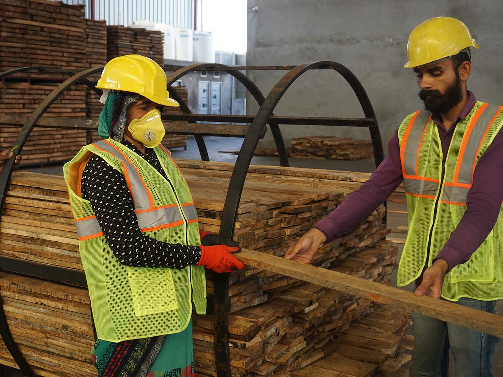 Two team members in full protective equipment lifting a sawn board together
