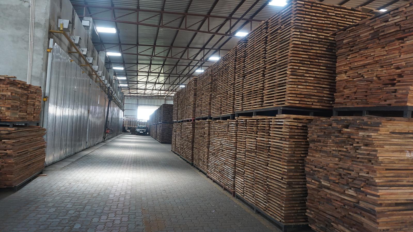 Covered timber store with stacked sawn boards alongside a row of seasoning chambers